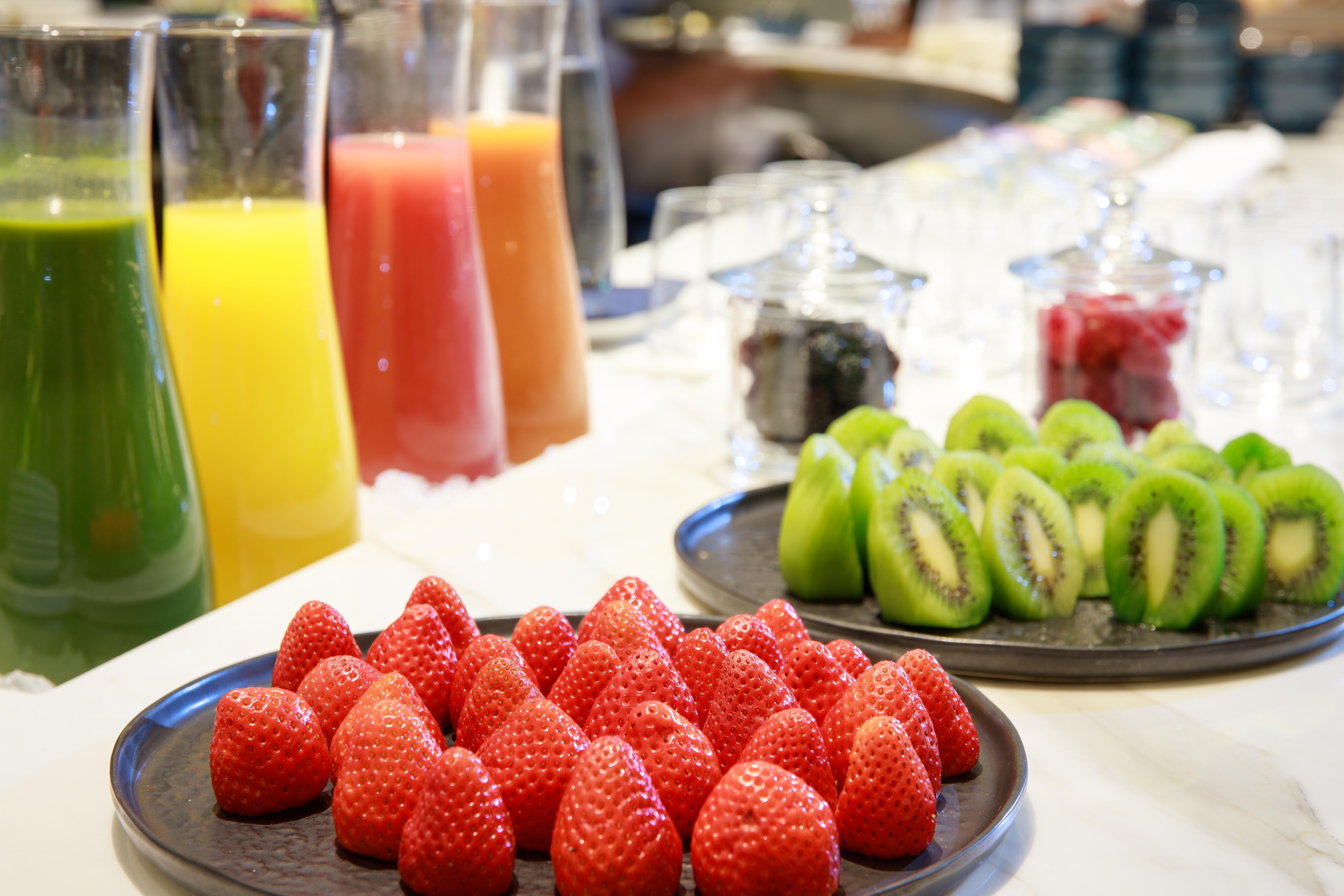 巴塞罗那索菲亚酒店-凯悦无限精选 外观 照片 The photo displays a vibrant assortment of fresh fruits and juices. In the foreground, there is a plate of bright red strawberries neatly arranged. Behind the strawberries, there are several tall glasses filled with various juices, including orange, 