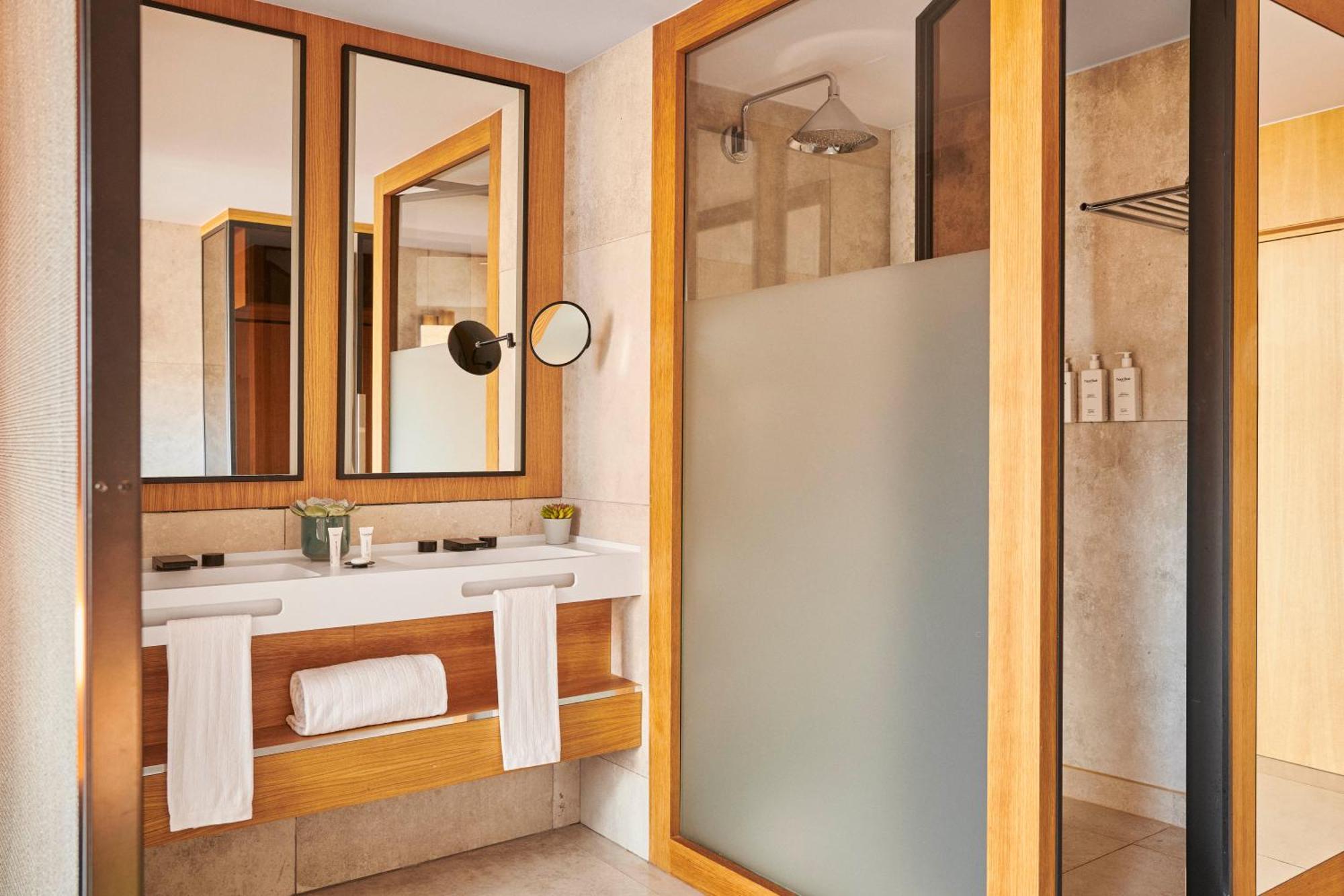 巴塞罗那索菲亚酒店-凯悦无限精选 外观 照片 The photo depicts a modern bathroom featuring a combination of natural materials and sleek design. There are three mirrors mounted on the wall above a wooden vanity. The vanity includes a basin and is adorned with toiletries and a small plant. On the