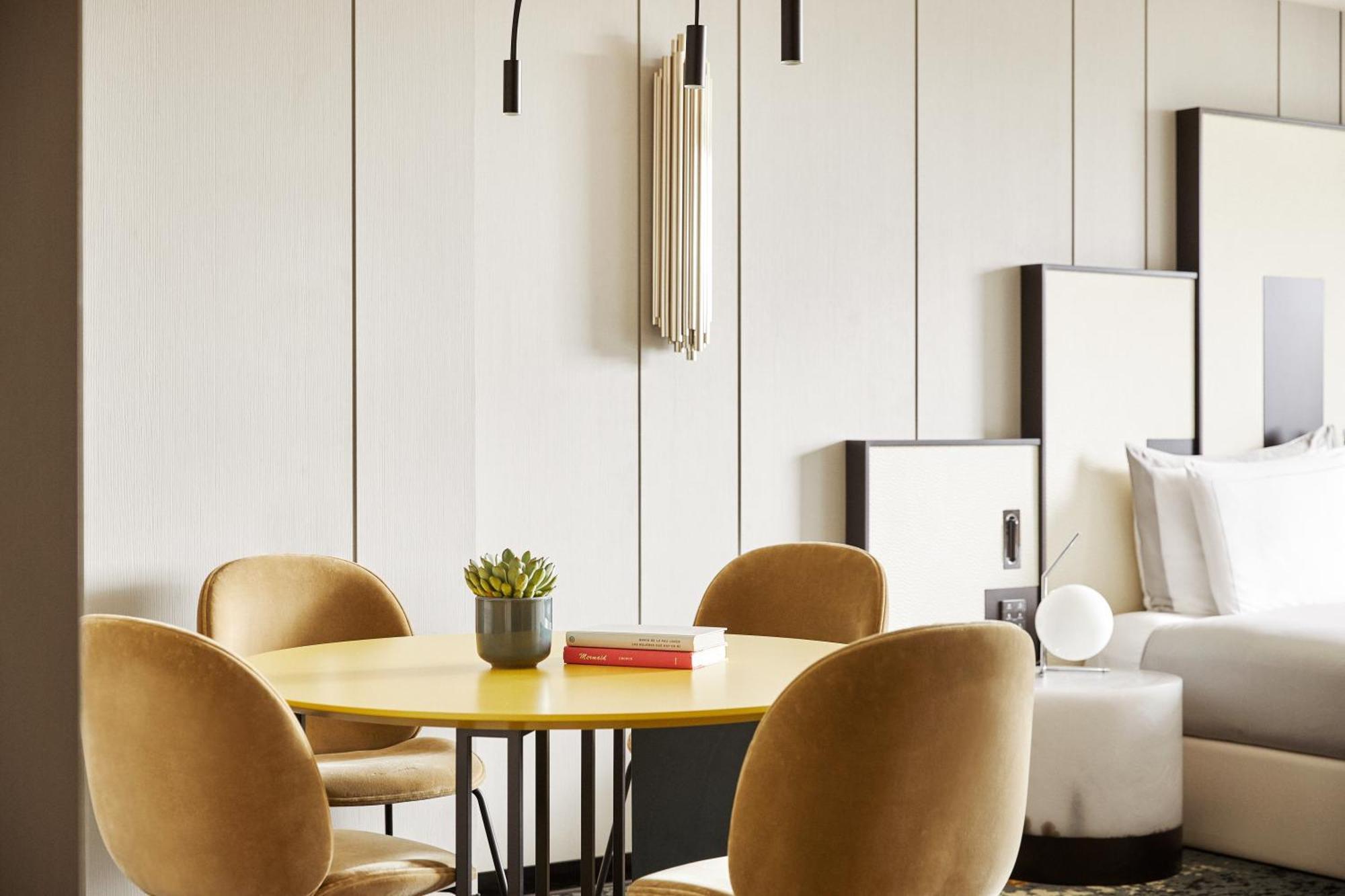 巴塞罗那索菲亚酒店-凯悦无限精选 外观 照片 The photo shows a modern interior setting, featuring a round yellow dining table with four comfortable, curved velvet chairs in a muted color. On the table, there is a small potted plant and a red book. The background features a light-colored wall wi