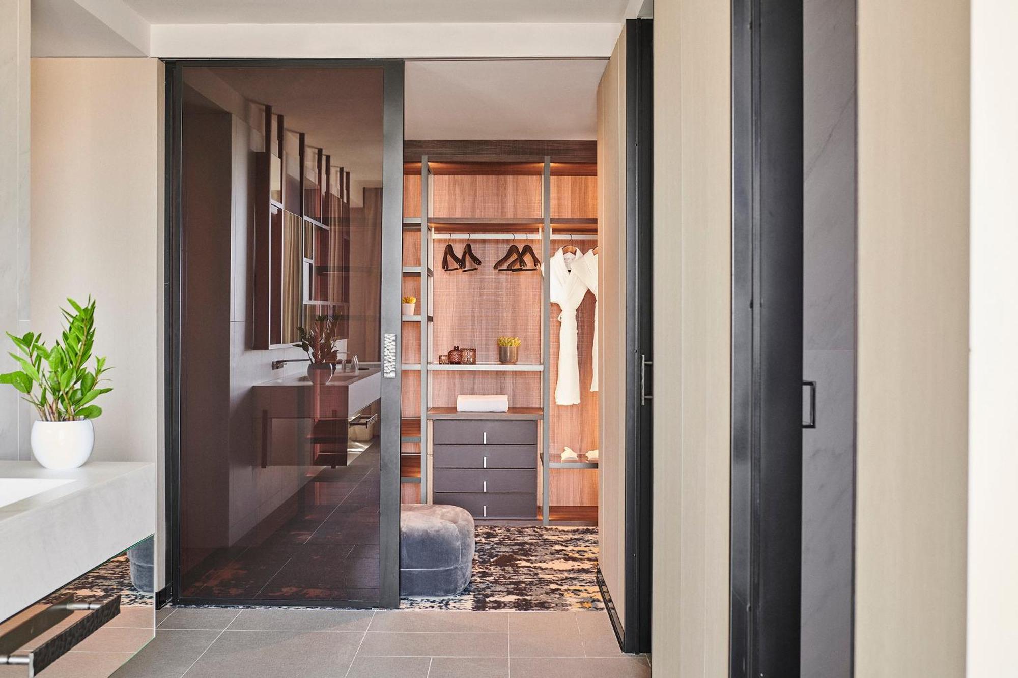 巴塞罗那索菲亚酒店-凯悦无限精选 外观 照片 The photo shows a modern and stylish interior space, likely a bedroom or a dressing area. In the foreground, there is a glass door leading into a closet. The closet has a wooden interior with hanging clothes, including several garments on hangers. Th